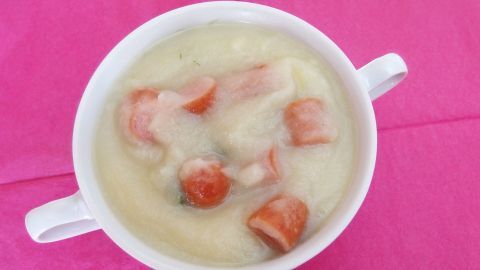 Eine cremige Kartoffelsuppe mit kleinen Wurststücken in einer weißen Schüssel auf einem pinken Tischläufer.
