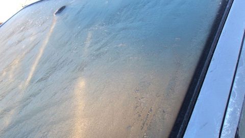 Eine gefrorene Windschutzscheibe zeigt Eisbildung, die im frühen Morgenlicht schimmert, bereit zum Auftauen.