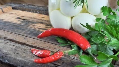 Soleier im Glas ruhen auf einem Holztisch neben frischen roten Chilis und grünem Petersilienkraut, dekorativ arrangiert.
