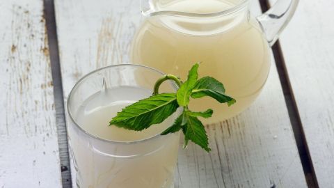 Ein Glas Gerstenwasser steht auf einem Tisch, während ein Krug mit dem erfrischenden Getränk daneben platziert ist.