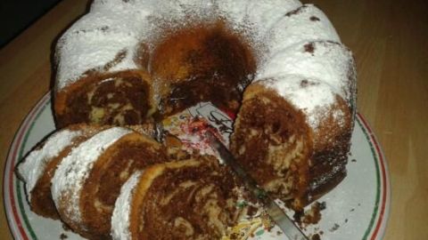 Ein Marmorkuchen liegt auf einem Teller, teilweise geschnitten und mit Puderzucker bestreut, in einer gemütlichen Küchenumgebung.