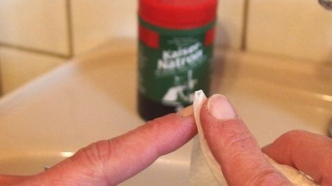 Eine Hand entfernt Druckertinte von einem Fingernagel mit einem Tuch, während eine Flasche im Hintergrund steht.