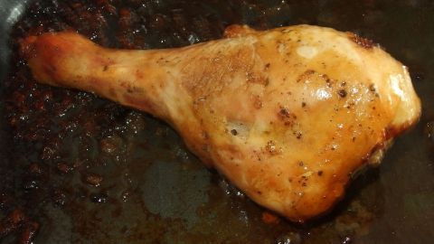 Ein knuspriges Hähnchenschenkel liegt in einer Bratpfanne, umgeben von dunklem Bratensaft, bereit zum Servieren.