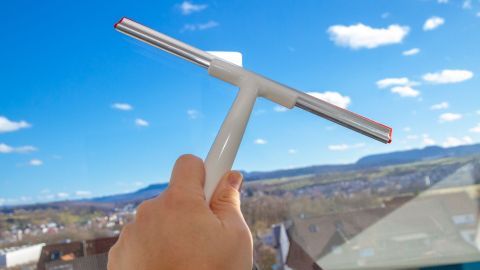 Ein Fensterwischer wird benutzt, um ein Fenster zu reinigen, während die Aussicht auf eine klare Himmelslandschaft zu sehen ist.