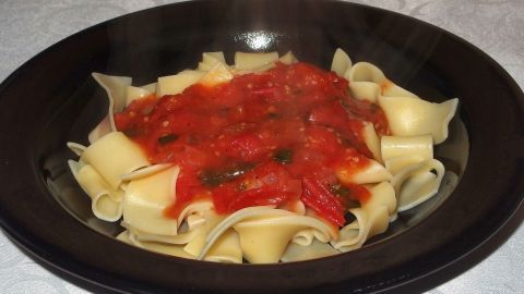 Ein Teller mit Bandnudeln ist mit einer appetitlichen Tomatensauce bedeckt, umgeben von einem dunklen Geschirr.