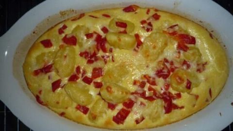 Ein Auflauf mit Gnocchi und roten Paprikastücken wird goldbraun gebacken und befindet sich in einer weißen Auflaufform.
