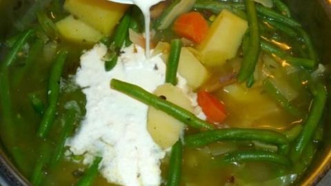 Eine cremige Gem&uuml;sesuppe mit Kartoffeln und Bohnen wird zubereitet, w&auml;hrend Sahne &uuml;ber die bunten Zutaten gegossen wird.
