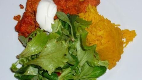 Hühnerbrust in Joghurt-Tandoori-Sauce auf einem Teller, serviert mit Curcuma-Reis und frischem Salat.