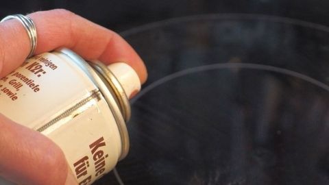 Eine Hand hält eine Sprühdose mit Backofenreiniger über ein Glaskeramik Kochfeld, um es zu reinigen.