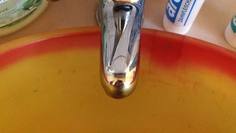 Ein Wasserhahn mit fließendem Wasser über einem orangefarbenen Spülbecken, umgeben von Reinigungsmitteln.