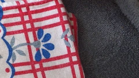 Ein Teppichboden zeigt Abdrücke von Möbeln, während ein dekoratives Tuch mit rotem Karomuster daneben liegt.