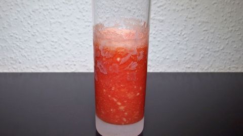 Ein erfrischender Himbeer-Bananen-Mango Smoothie füllt ein hohes Glas, das auf einem dunklen Tisch steht.