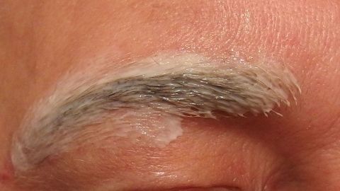 Ein Augenbraue wird mit einer Zupf-Creme behandelt, um das Zupfen so gut wie schmerzlos zu gestalten.