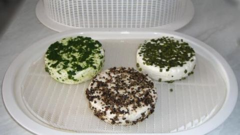 Drei frisch zubereitete Frischkäse-Rollen liegen auf einem Abtropfgitter, garniert mit Kräutern.