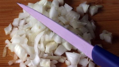 Zwiebeln schneiden kann eine heikle Angelegenheit sein, aber mit den richtigen Tipps vermeidest du Tränen. Diese gepellten und fein geschnittenen Zwiebeln zeigen, dass es einfacher geht, als du denkst. Lerne die besten Tricks dafür! Gehackte Zwiebeln liegen auf einem Holzbrett, während ein lila Messer daneben zum Schneiden bereitsteht.