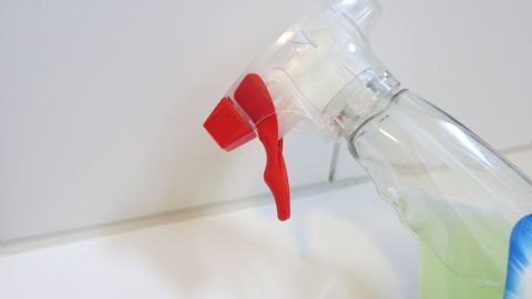 Eine Sprühflasche mit rotem Sprühkopf wird in Richtung einer gefliesten Wand gehalten, um Silikonfugen zu reinigen.