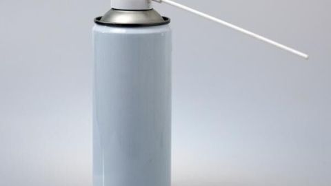 Eine weiße Silikonspraydose mit langem Sprührohr steht auf einer glatten Oberfläche in einem neutralen Umfeld.
