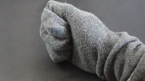 Eine graue Socke-Handschuh wird zusammengedrückt, um die eingecremten Hände nachts zu schützen und zu befeuchten.