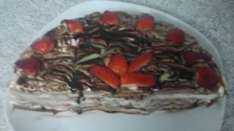 Eine Erdbeer-Bananen-Joghurt-Quark-Torte liegt auf einem weißen Teller, dekoriert mit frischen Erdbeeren und Schokoladensauce.