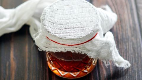 Ein Glas mit Whisky ist mit einem Tuch bedeckt, um Fruchtfliegen zu fangen, auf einer Holzoberfläche platziert.