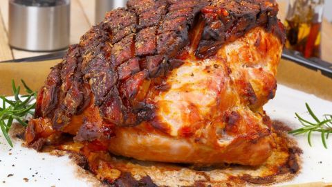 Saftiger Schweinebraten liegt auf einem Teller, perfekt gebraten mit knuspriger Kruste, umgeben von Kräutern.