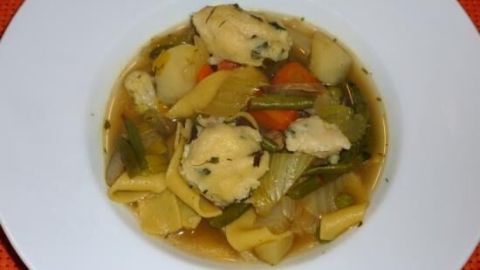 Eine Schüssel Gemüsesuppe zeigt fluffige Grießnocken mit Käse, umgeben von buntem Gemüse und Brühe, auf einem weißen Teller.