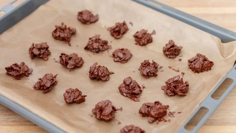 Klappt mit weißer, Milch- und Zartbitterschokolade und kommt in einer netten Tüte auch gut als Geschenk. Kleine schokoladige Knuspersnacks liegen auf einem Backblech mit Backpapier, bereit zum Ausbacken oder Abkühlen.