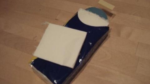 Ein Paket Taschentücher liegt auf einem Holztisch, daneben ein einzelnes Taschentuch. Der Kontext ist ein heller Raum.