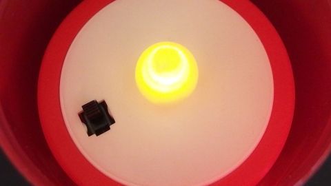 Eine LED-Kerze leuchtet in Gelb und erzeugt eine gemütliche Atmosphäre in einem runden, roten Kerzenhalter.