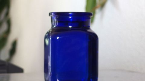 Ein blauer Glasbehälter steht auf einem Tisch, umgeben von einer minimalistischen Umgebung, die Sinne anregt.