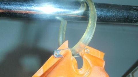 In diesem Bild siehst du einen beschädigten Duschvorhang mit abgerissenem Loch, das an einem Duschvorhangring hängt. Im Artikel findest du hilfreiche Tipps, wie du solche Schäden einfach selbst reparieren kannst. Ein orangefarbener Duschvorhang hängt an einem Duschstangenring, der an einer glänzenden Stange befestigt ist.