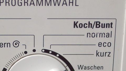 Das Bedienfeld einer Waschmaschine zeigt verschiedene Waschprogramme wie "Koch/Bunt" an, während der Nutzer eine Auswahl trifft.