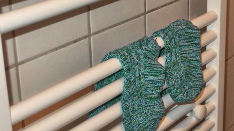 Auf einem Heizkörper liegen zwei grüne Socken, die sich in einem Badezimmer-Kontext erwärmen.