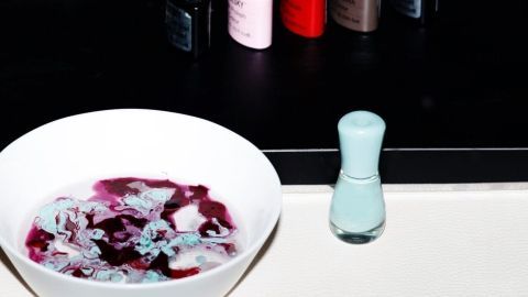 In einer weißen Schüssel schwimmt eine farbige Nail Art-Wasseroberfläche, während Nagellackflaschen im Hintergrund stehen.