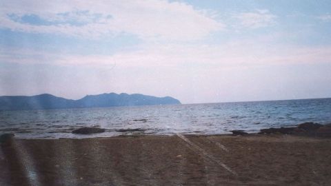 Ein schöner Strand erstreckt sich vor dem ruhigen Meer, das sanft gegen die Ufersteine plätschert, unter einem blauen Himmel.