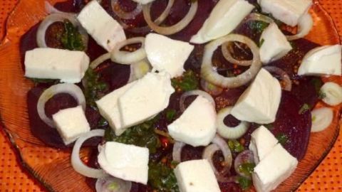 Rote Beete-Scheiben mit Mozzarella und Zwiebeln liegen dekorativ auf einem orangefarbenen Teller.