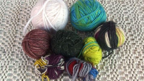 Originelle Geschenkbänder aus Wollresten herstellen. Bunte Wollreste liegen auf einem hellen Untergrund, bereit zur Verarbeitung für originelle Geschenkbänder.