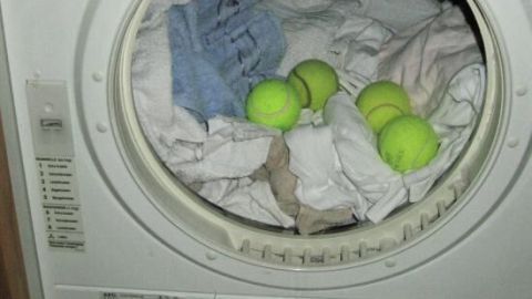 Eine Wäschetrockner-Trommel mit sauberen, gewaschenen Kleidungsstücken und sechs grünen Tennisbällen im Inneren.