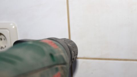Eine bohrmaschine zielt präzise auf eine Fliese, um punktgenau zu bohren, während eine Steckdose im Hintergrund sichtbar ist.