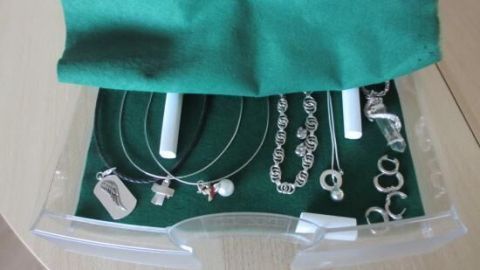 Schmuck wie Ketten und Anhänger liegt ordentlich in einer transparenten Schubladenbox mit grünem Stoffeinsatz auf Holztisch.