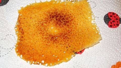 Ein Käsecracker liegt auf einem Küchenpapier, leicht goldbraun und knusprig, nach der Zubereitung in der Mikrowelle.
