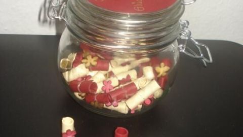 Ein Glas voller bunter Zettel mit Glücksmomenten ist offen auf einem Tisch, umgeben von weiteren Zetteln.