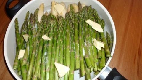 Grüner Spargel liegt in einem Topf mit etwas Wasser und Stückchen Butter, bereit für die Zubereitung.