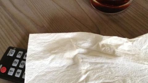 Eine Fernbedienung liegt auf einem Tisch, mit einem Papiertuch daneben, während Cola in einem Glas steht.