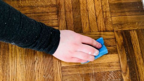 Wachsflecken auf dem Parkett kannst du entfernen, indem du sie mit Speiseöl einreibst. Ein Handtuch wischen einen Wachsfleck auf einem Parkettboden, um den Holzfußboden zu reinigen und zu pflegen.