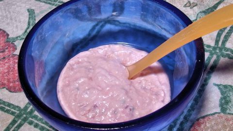 Ein blauer Schüssel enthält frisch zubereiteten Babybrei, während ein Löffel bereit zum Servieren daneben liegt.