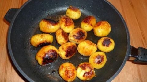 Karamellisierte Kartoffeln bräunen in einer Pfanne, umgeben von Holzoberfläche, perfekt für eine köstliche Beilage.