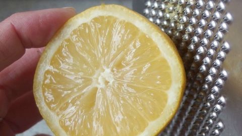 Eine Hand hält eine geschnittene Zitrone, während sie über eine Raffel geführt wird, um Zitronenschalenabrieb zu gewinnen.