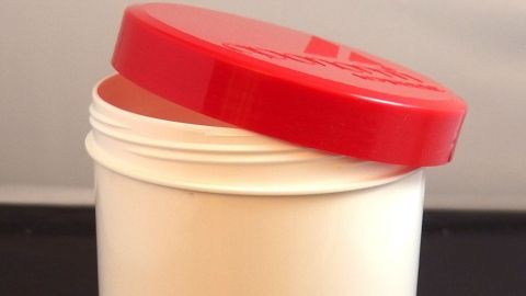 Eine weiße Schraubdose mit rotem Deckel steht geöffnet auf einem Tisch, bereit zur Verwendung in einer Apotheke.