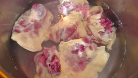 Teigtaschen aus Nudelteig mit roter Bete und Frischkäse werden im Wasser gekocht. Sie schwimmen in einer metallenen Schüssel.